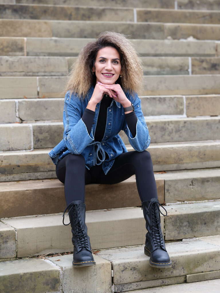 Eine mit Jeansjacke sitzt auf einer Treppe und stützt ihr Kinn auf ihre Hände.