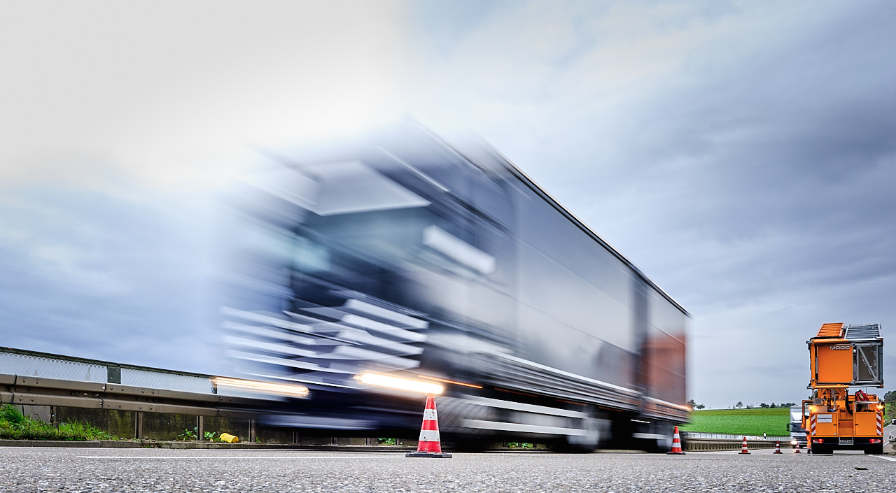 Ein Lkw braust an während einer Bauwerksprüfung an einem abgesicherten Brückenuntersichtsgerät vorbei