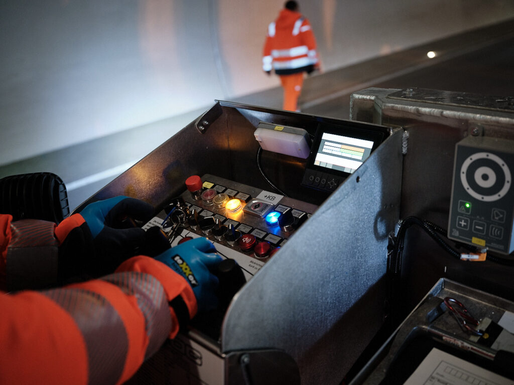 Bauwerksprüfung in einem Straßentunnel. Ein Techniker am Bediehnpult einer Arbeitsbühne. Aufnahme im Rahmen einer Unternehmensreportage zur Dokumentation technischer Infrastruktur.